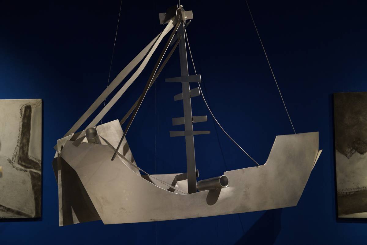 Massives 3D-Schiff aus glänzenden Aluplatten mit angedeutetem Masten und  Kanonenrohr vor blauem Hintergrund